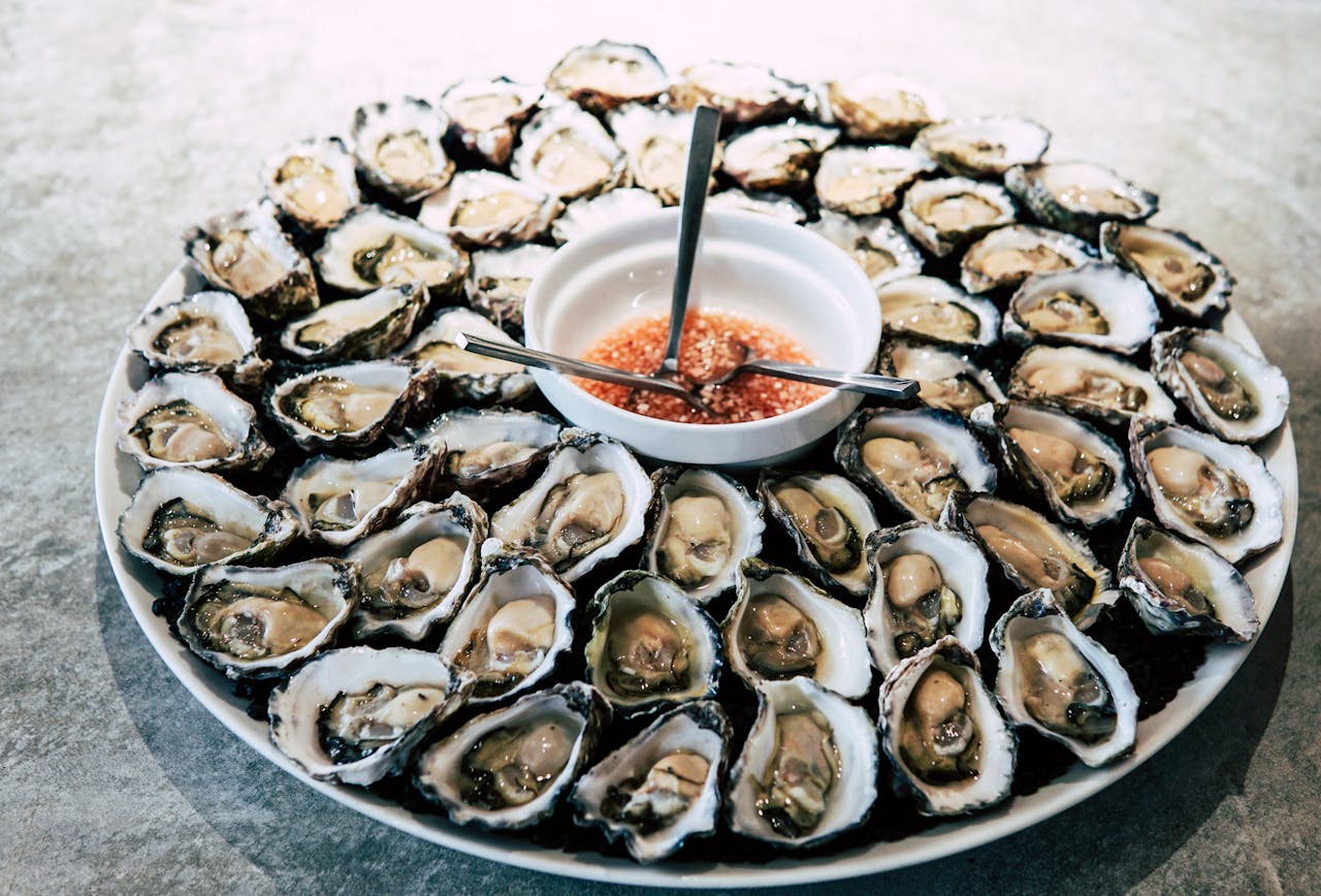 Services A stunning platter of fresh oysters with a tangy sauce, perfect for gourmet seafood enthusiasts.