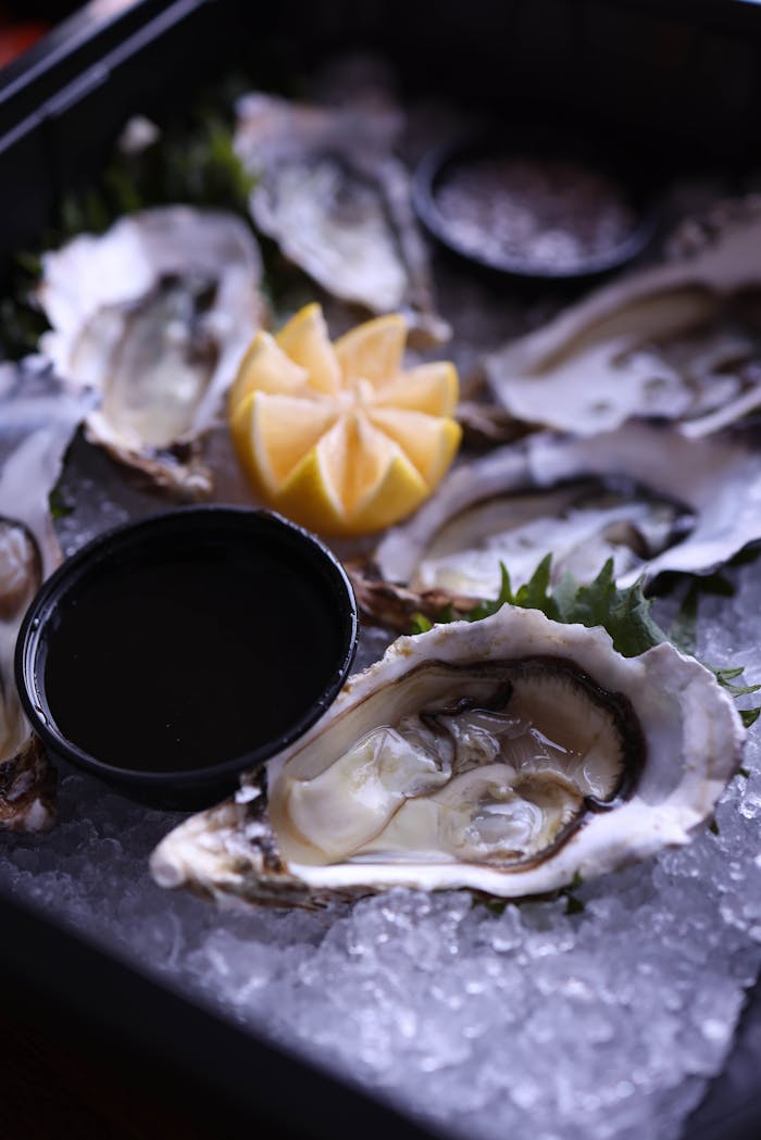 Services Close-up of fresh oysters on ice, served with lemon and sauce, perfect for seafood lovers.